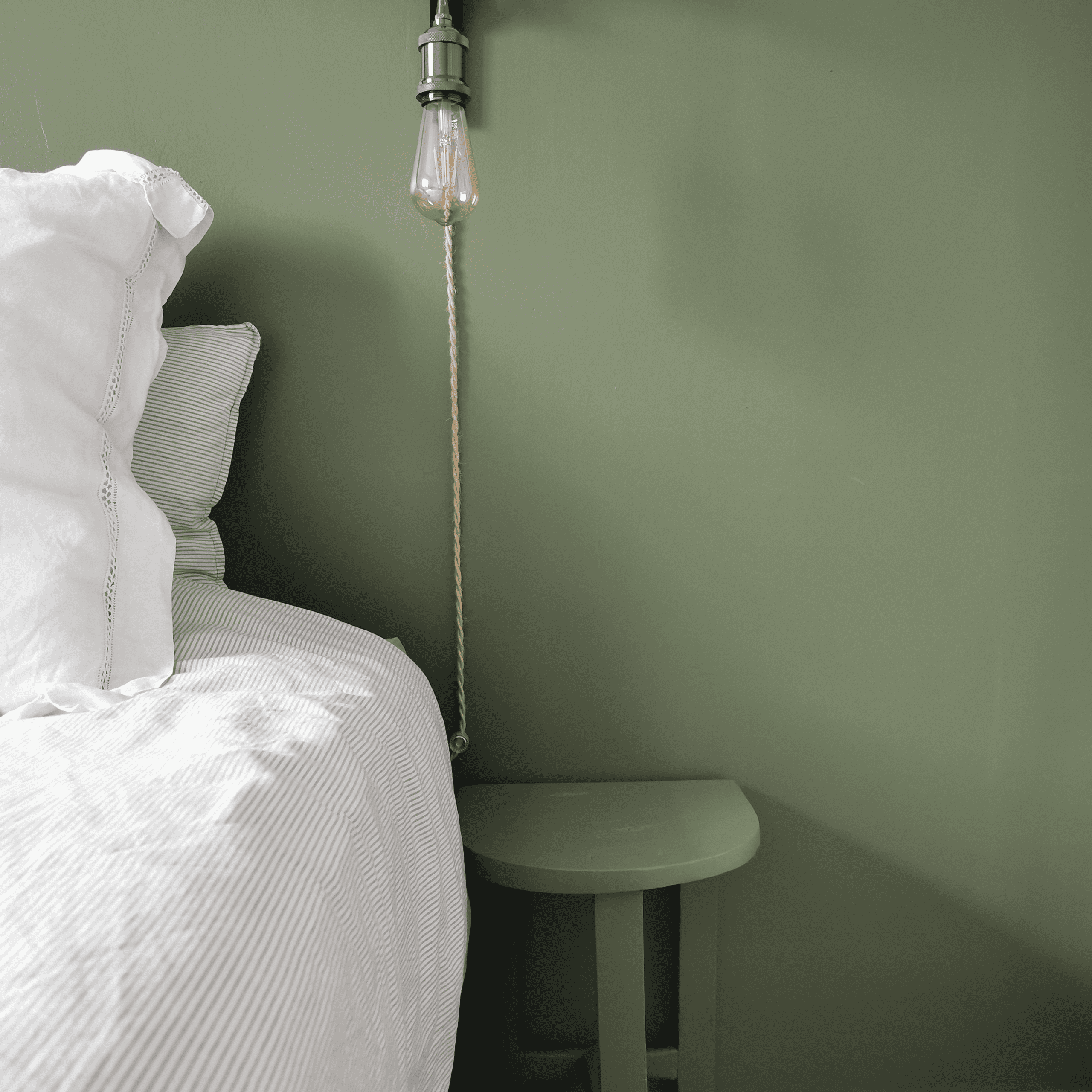 le côté d'un lit avec sa table de chevet assortie au mur de derrière qui est vert kaki